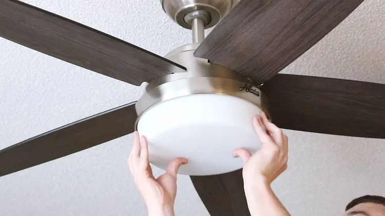 Professional technician installing a ceiling fan in a bedroom to help the air move better.