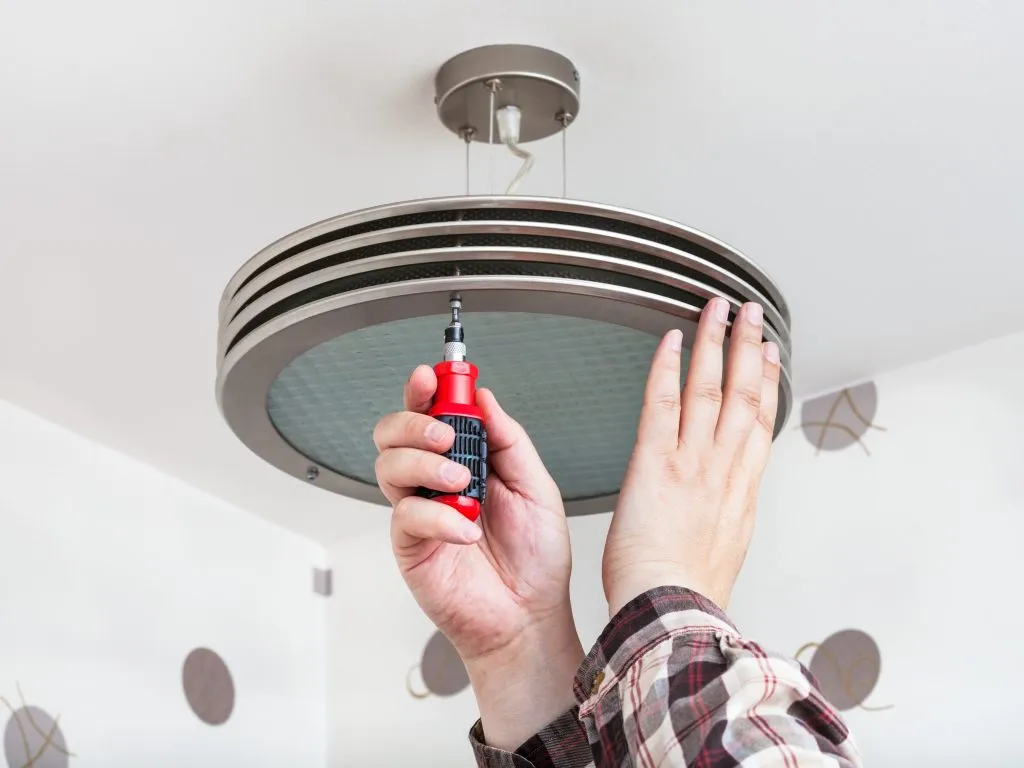 An electrician installing a modern light fixture to improve the home's décor.